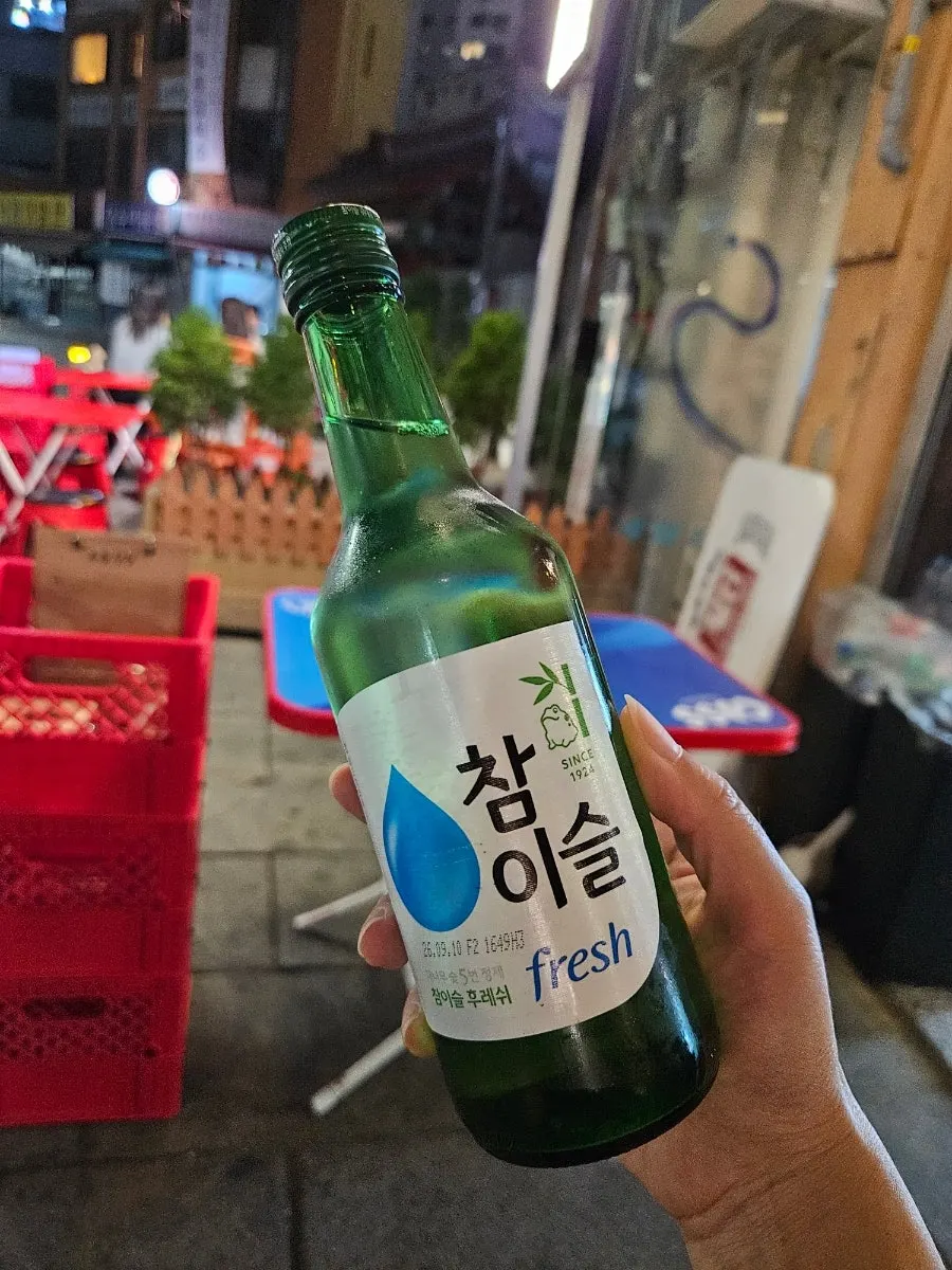A shot glass of soju beside meat grilling on the table
