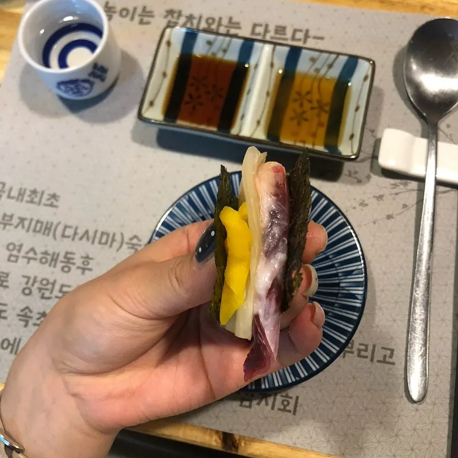 Sepotong sashimi tuna yang diangkat dengan sumpit