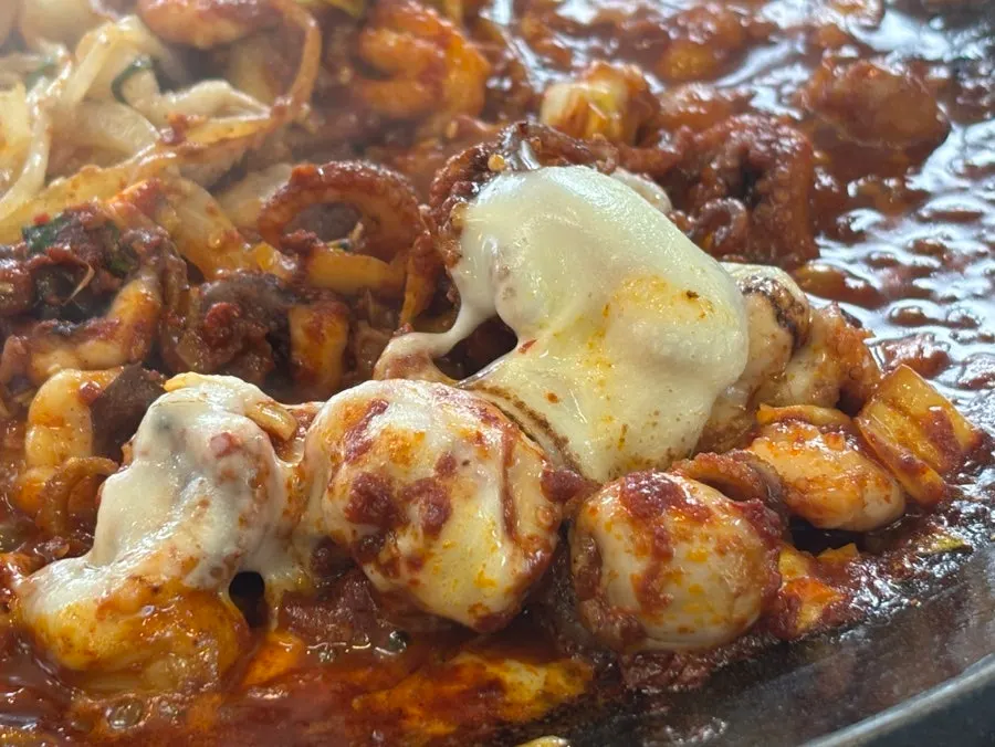 A bite of jjukkumi topped with pork belly