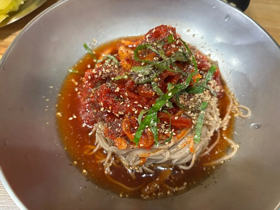 Spicy jjang kalguksu topped with egg, sesame seeds and seaweed flakes