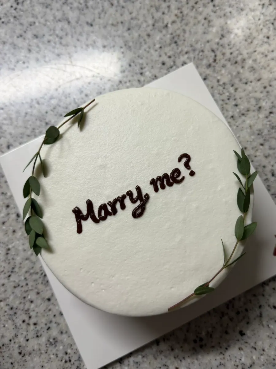 Front view of the white-toned lettering cake with eucalyptus decoration