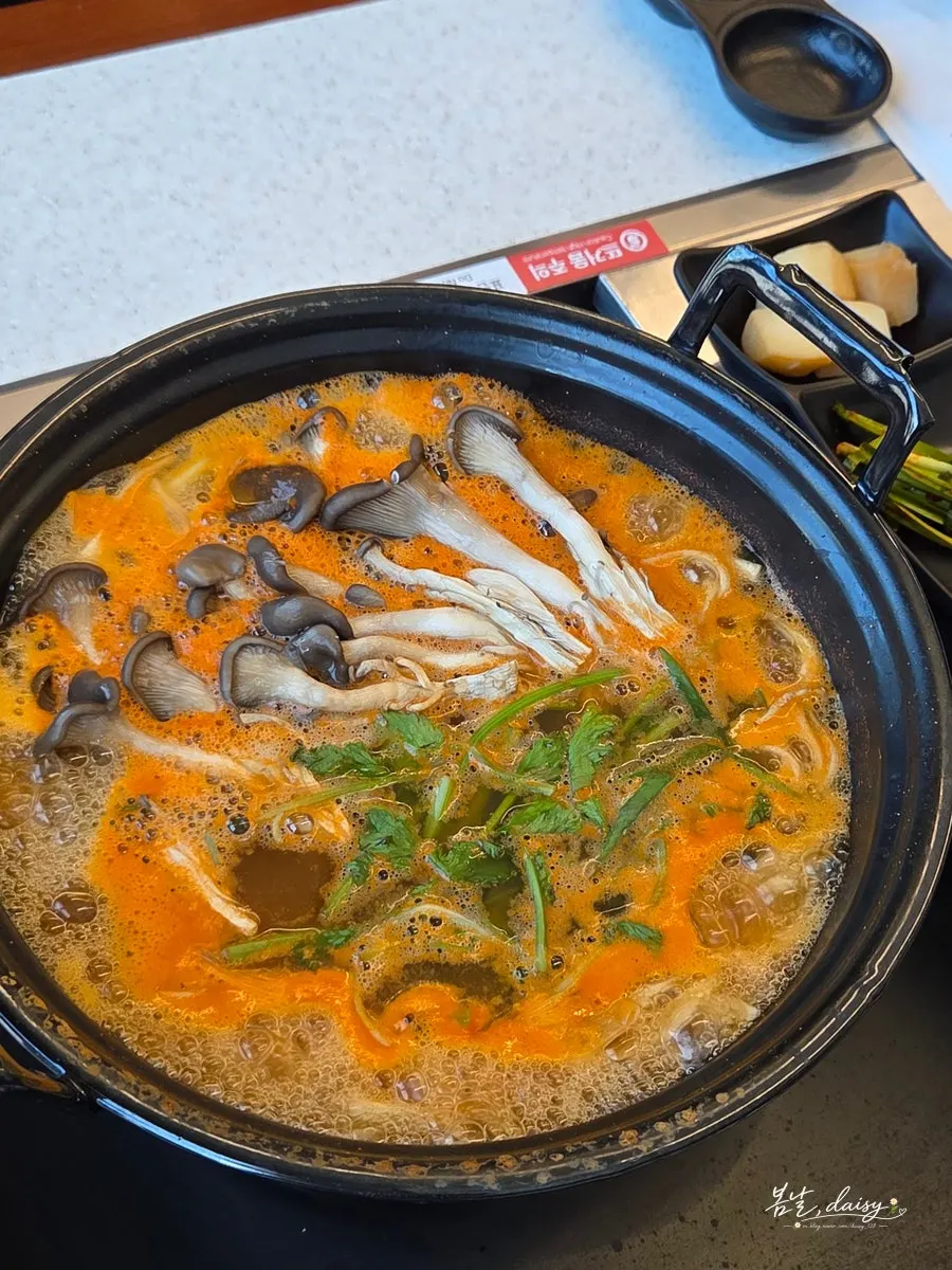 Pot of mushroom kalguksu topped with oyster mushrooms and minari