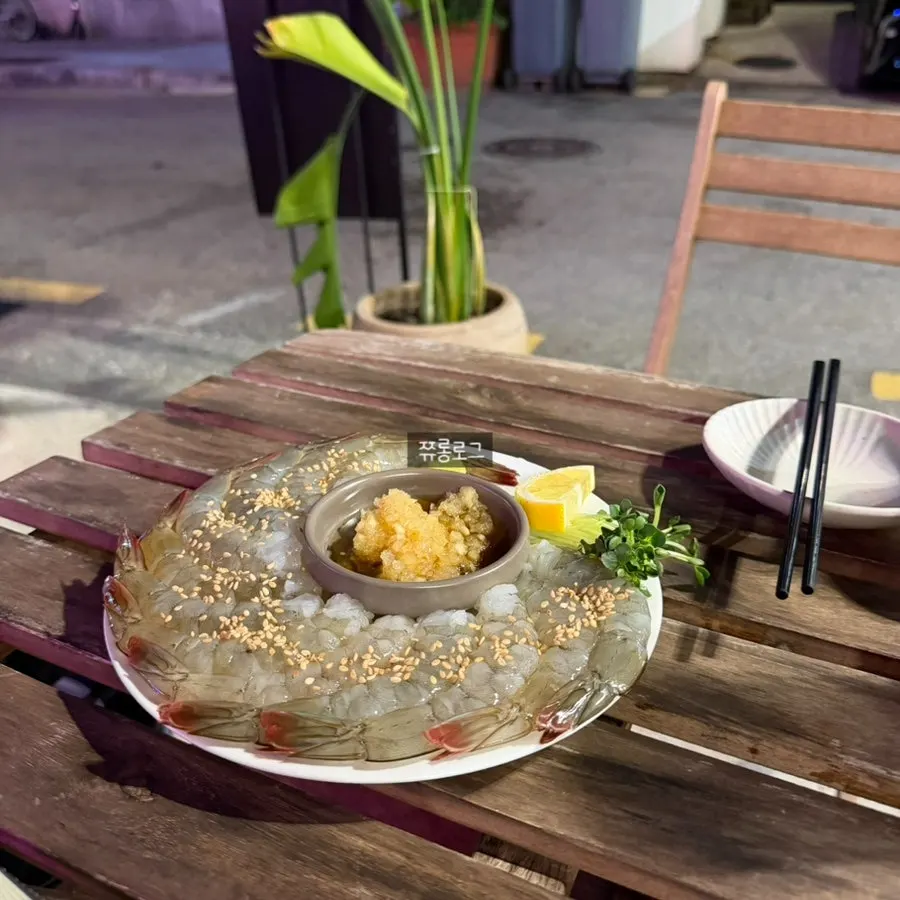 A single piece of raw shrimp sashimi held with chopsticks