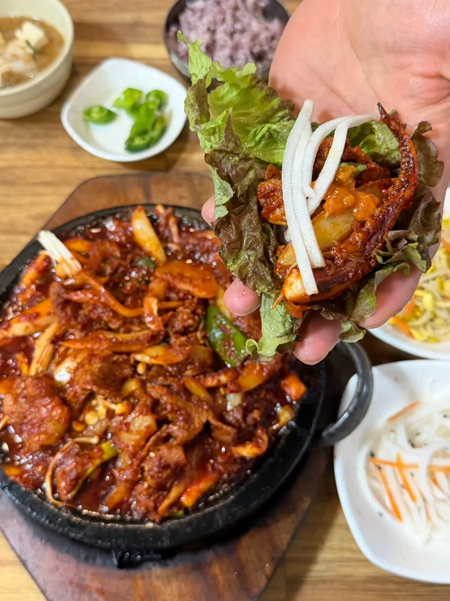 Hands wrapping ssam beside the stir-fry hot plate