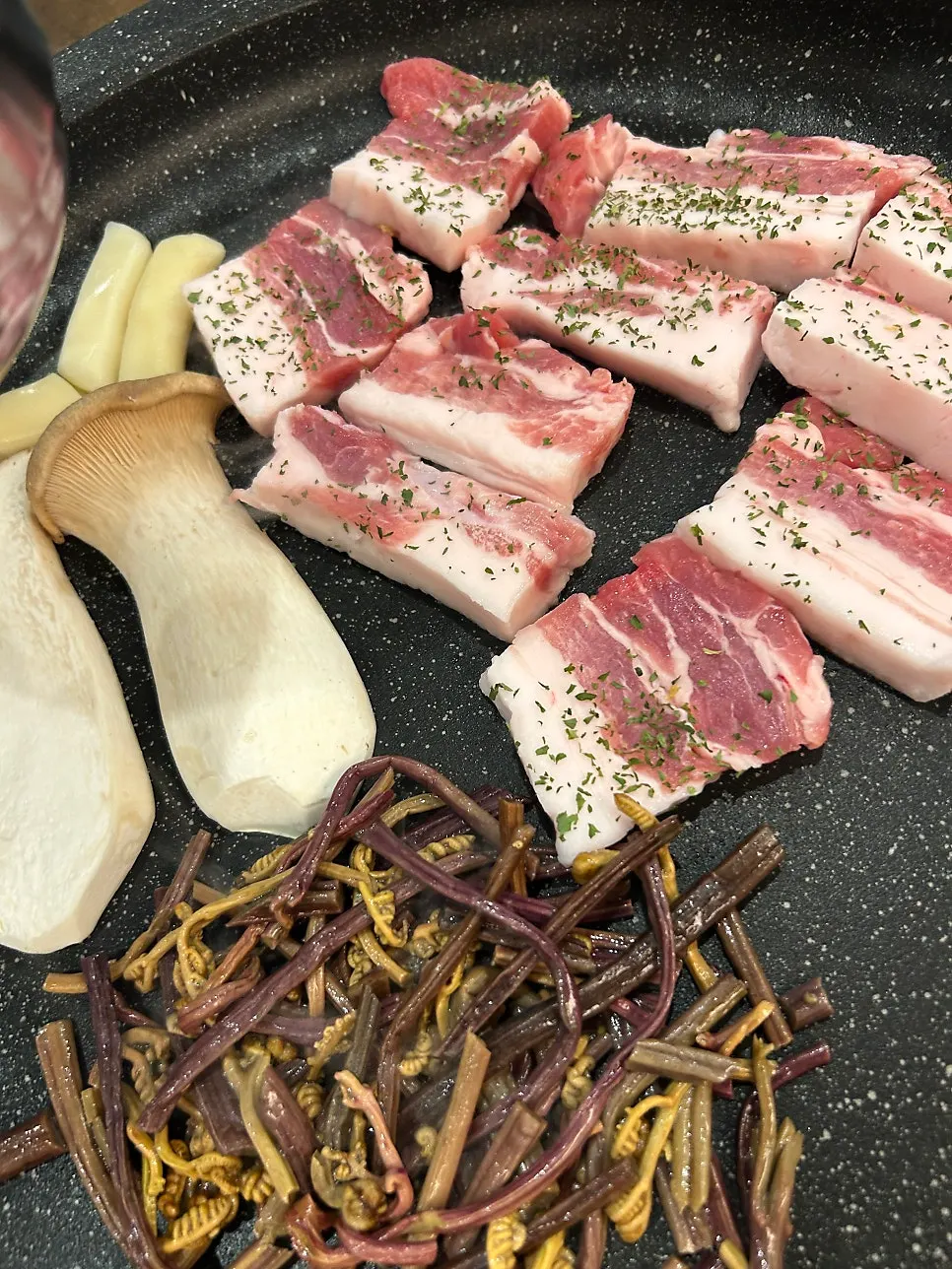 Fresh pork belly grilling with mushrooms, rice cake, and bracken fern
