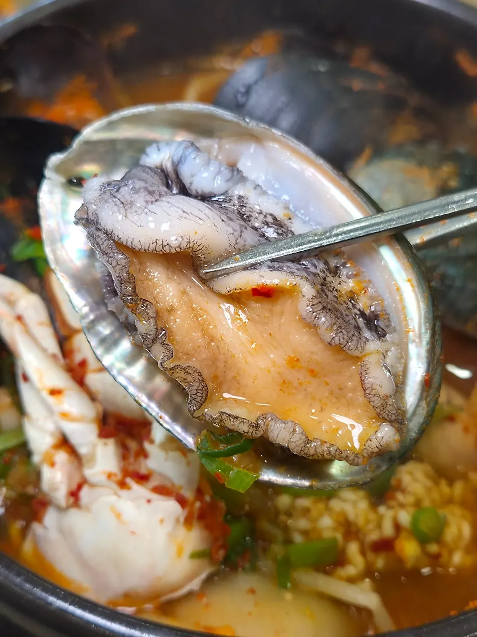 A bowl of seafood stew with whole live abalone