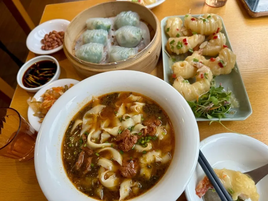 Table with a saucy dish, dumplings, and noodles together