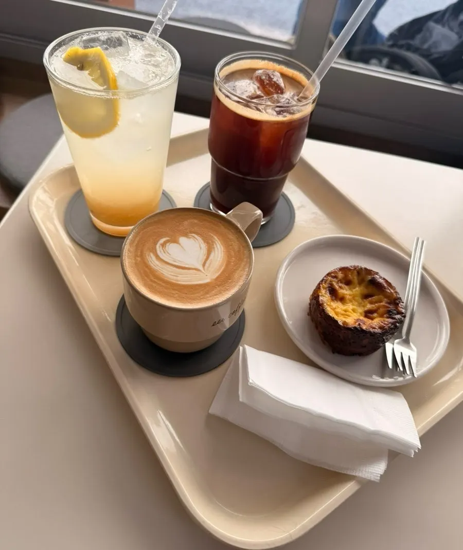 Almond latte, americano, lemonade and egg financier laid out together