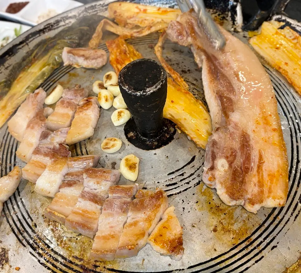 Pork belly and aged kimchi grilling on a cast-iron lid