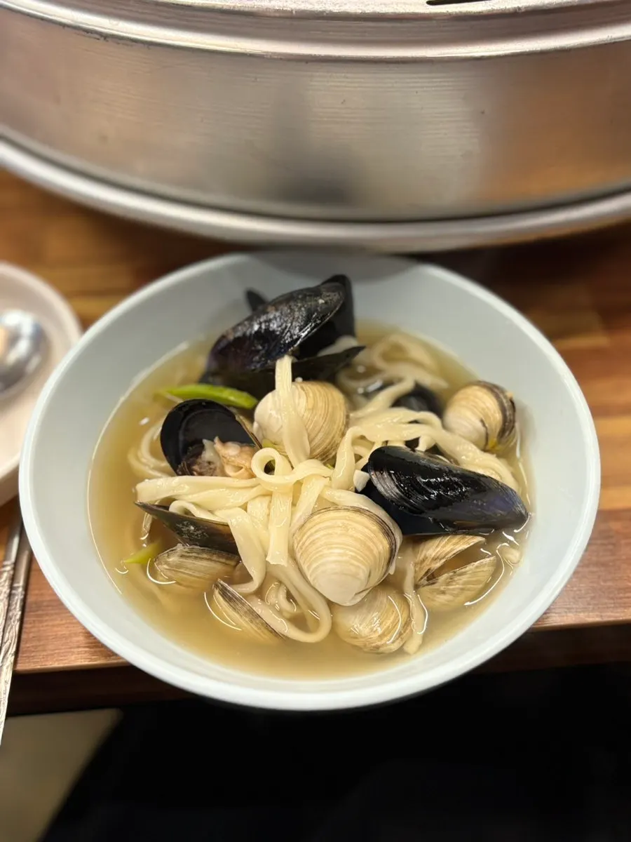 A pot of clam kalguksu topped with hard clams and mussels