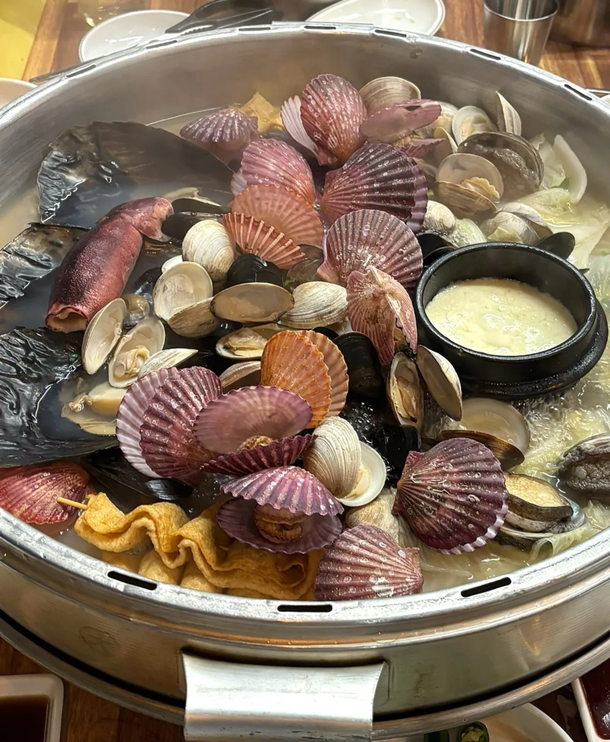 The lid removed to reveal clams and cheese packed into the hotpot