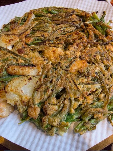 A piece of tasting-size seafood pajeon topped with kimchi