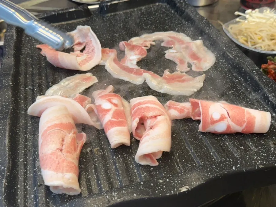 Thin-sliced pork belly cooking on the grill