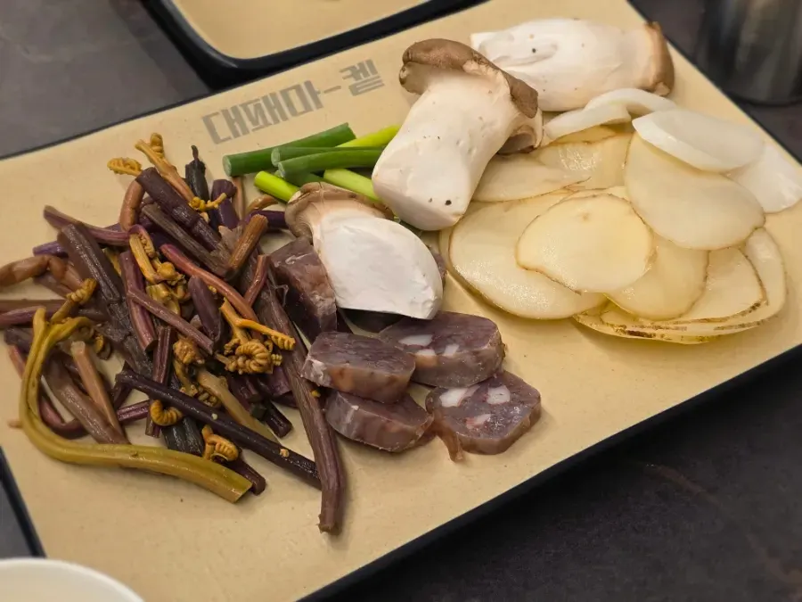 Plate of grilling sides including bracken, mushrooms, garlic scapes and potato