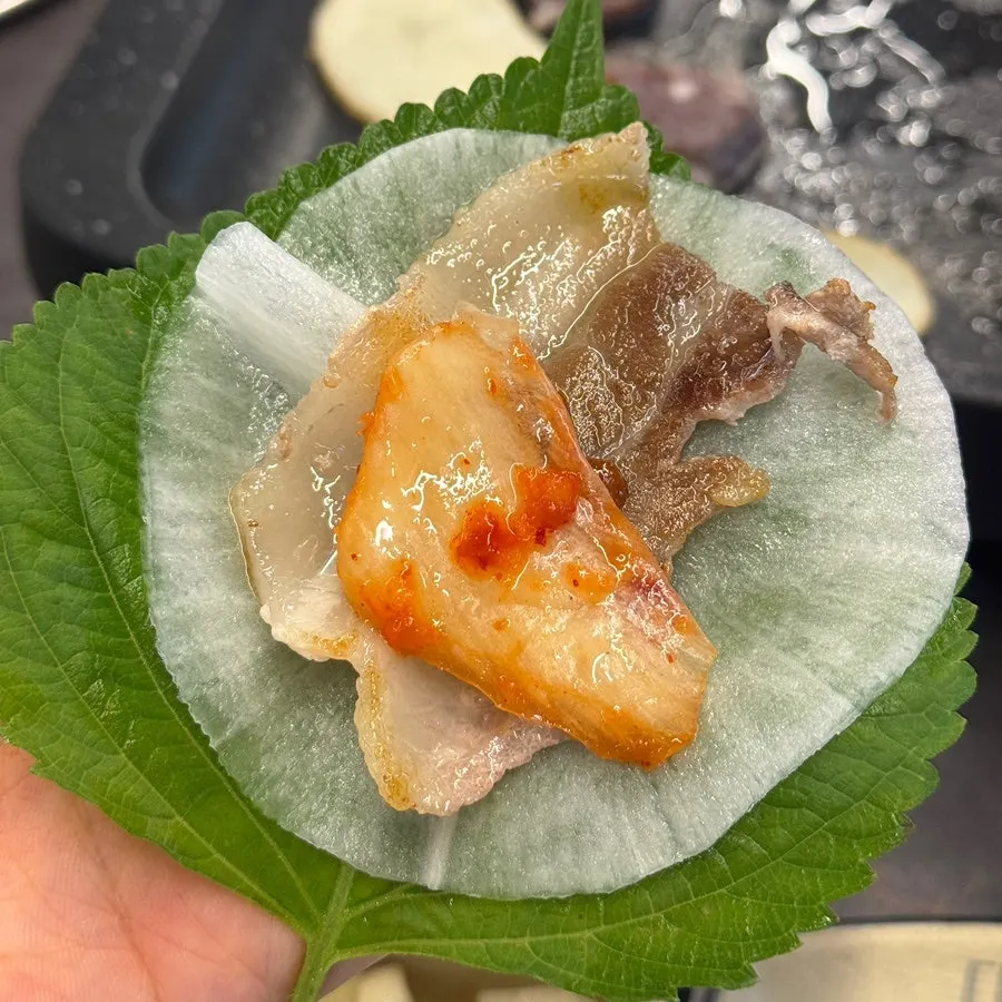 A piece of daepae samgyeopsal picked up with tongs