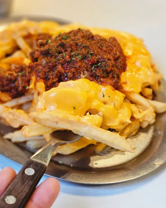 Lifting up the cheese sauce on the chili cheese fries