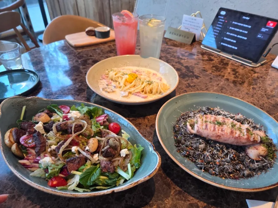 Table spread with beef steak salad, squid ink risotto, and carbonara