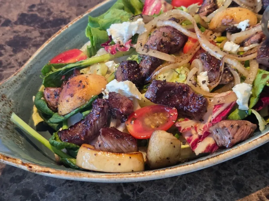 Beef steak salad served alongside pasta