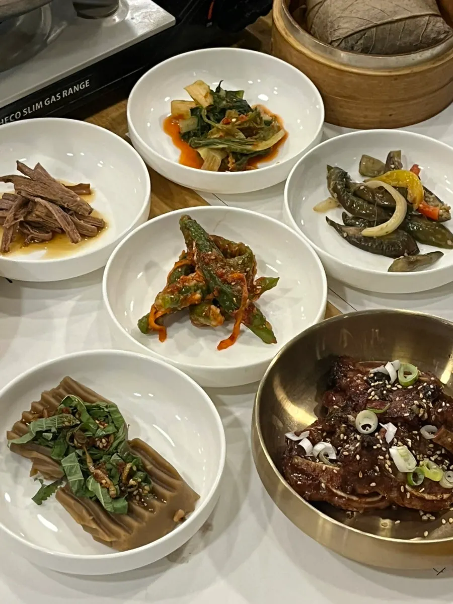 Side dishes of braised beef, pickled peppers, kimchi, and seasoned eggplant