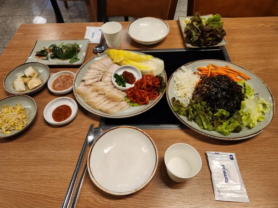 A table set with lettuce, perilla leaves, kimchi, and pickled radish side dishes