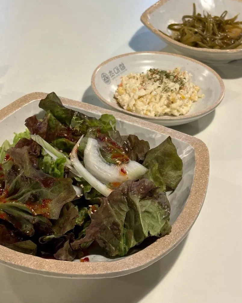 Table spread of basic side dishes: seasoned lettuce, corn salad, and pickled garlic scapes
