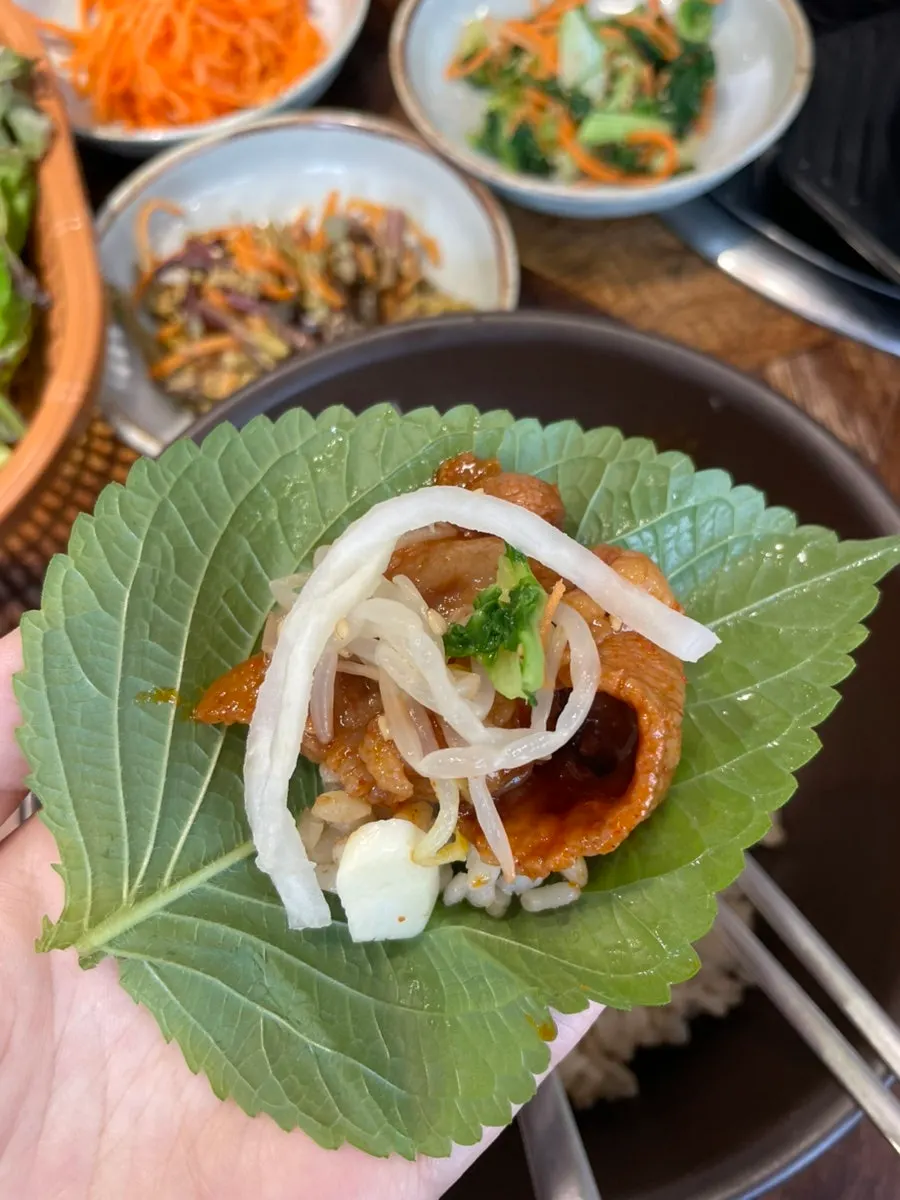A lettuce wrap filled with jeyuk and side dishes
