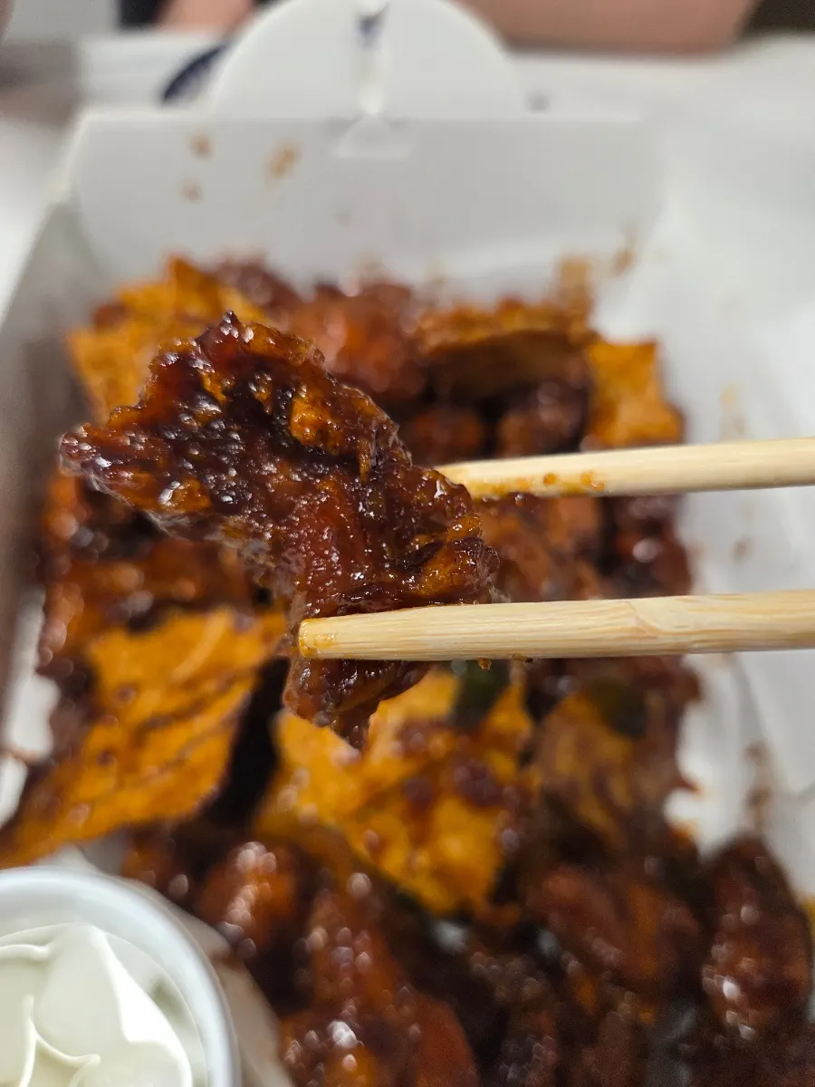 Chopsticks picking up a piece of black garlic dakgangjeong