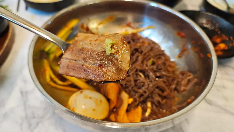 A bite of samgyeopsal topped with bibim naengmyeon