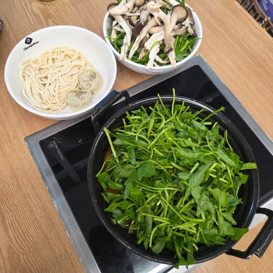 Pot of spicy mushroom kalguksu piled high with minari