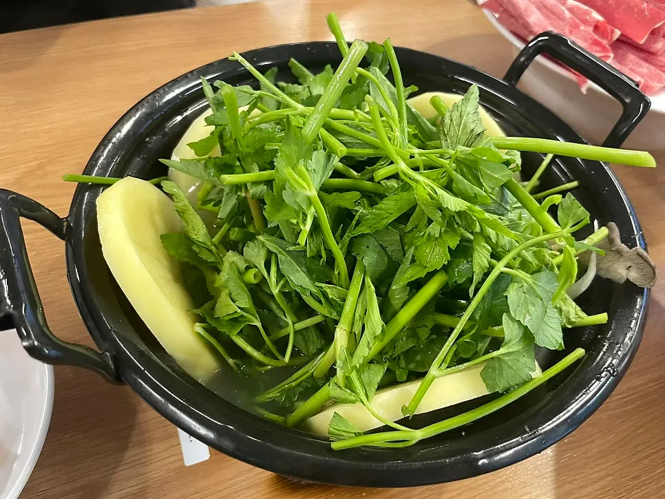 A full spread of clear mushroom shabu-shabu kalguksu piled high with minari