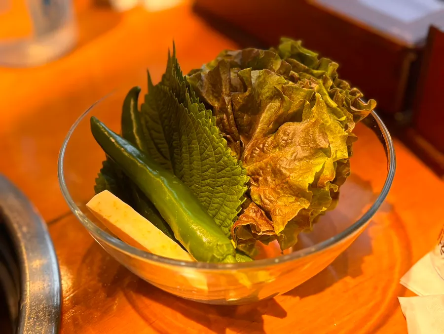 Sayuran lalap dengan daging dan irisan daun bawang di atasnya