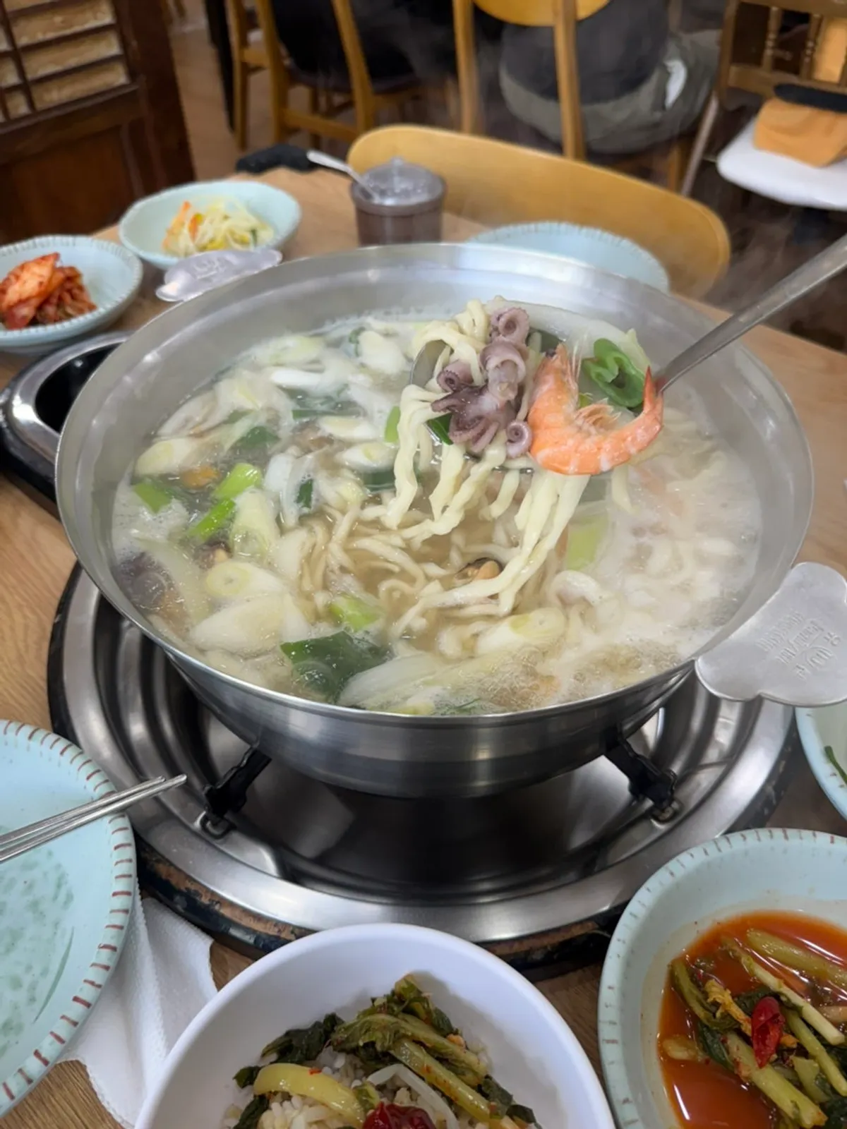 A pot of seafood kalguksu cooking with an hourglass