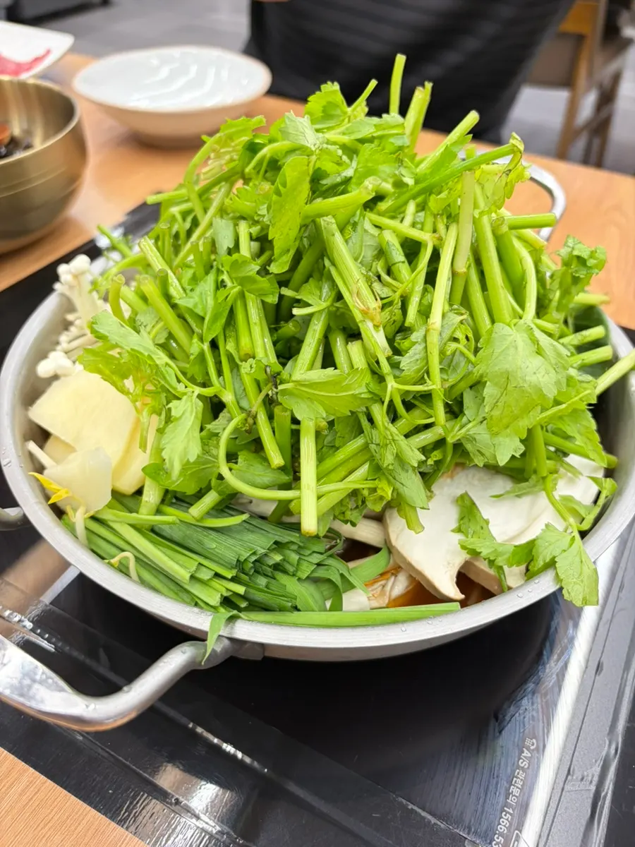 Pot of shabu kalguksu piled high with minari