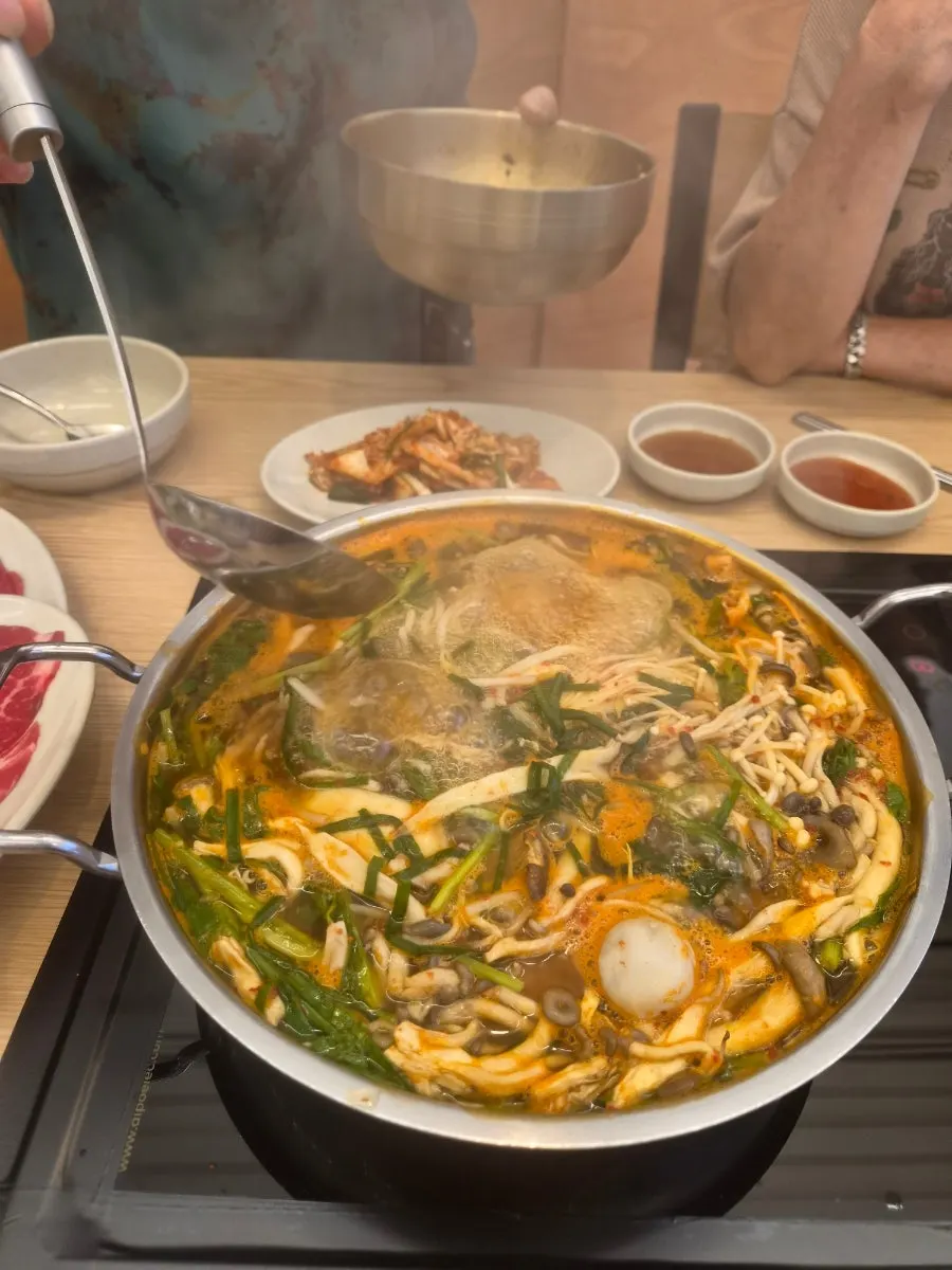 Pot of shabu-shabu boiling with mushrooms, potatoes, and minari