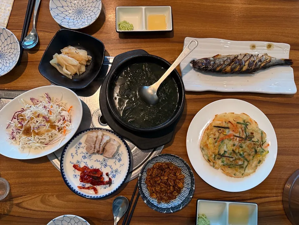 Banchan spread of grilled fish, seaweed soup, jeon and boiled pork