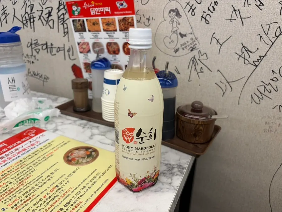Makgeolli glass alongside a full dak hanmari spread
