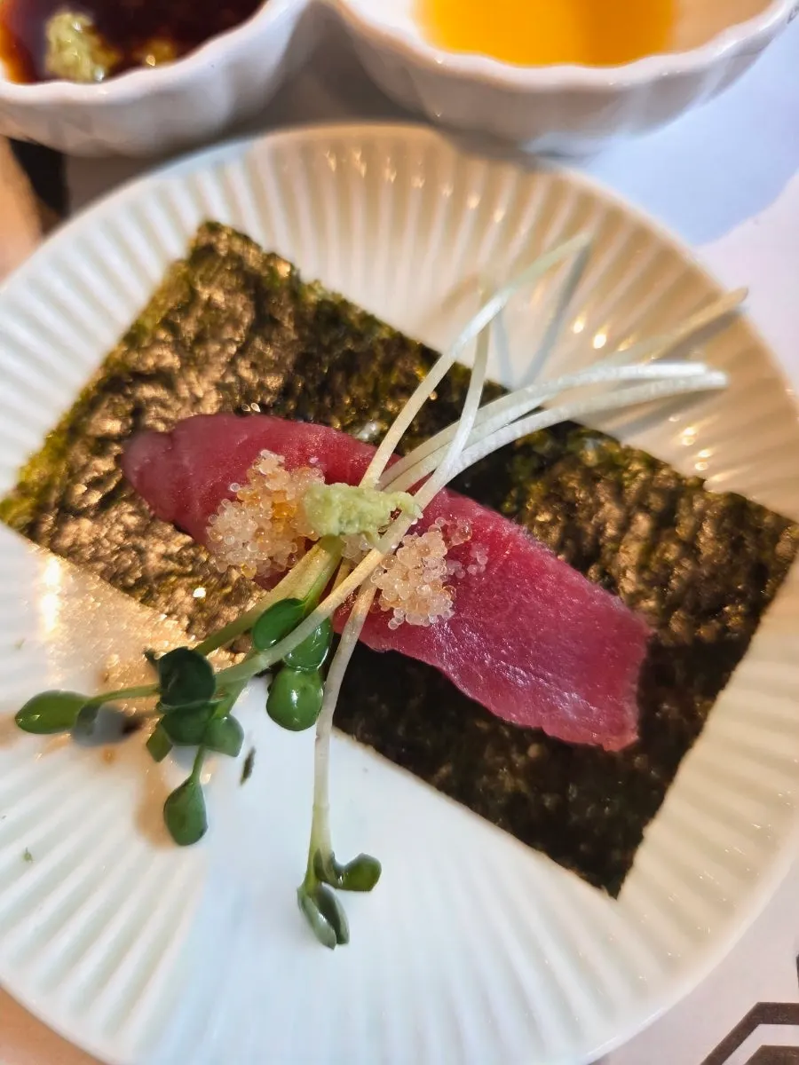 A single piece of aged tuna sashimi picked up with chopsticks