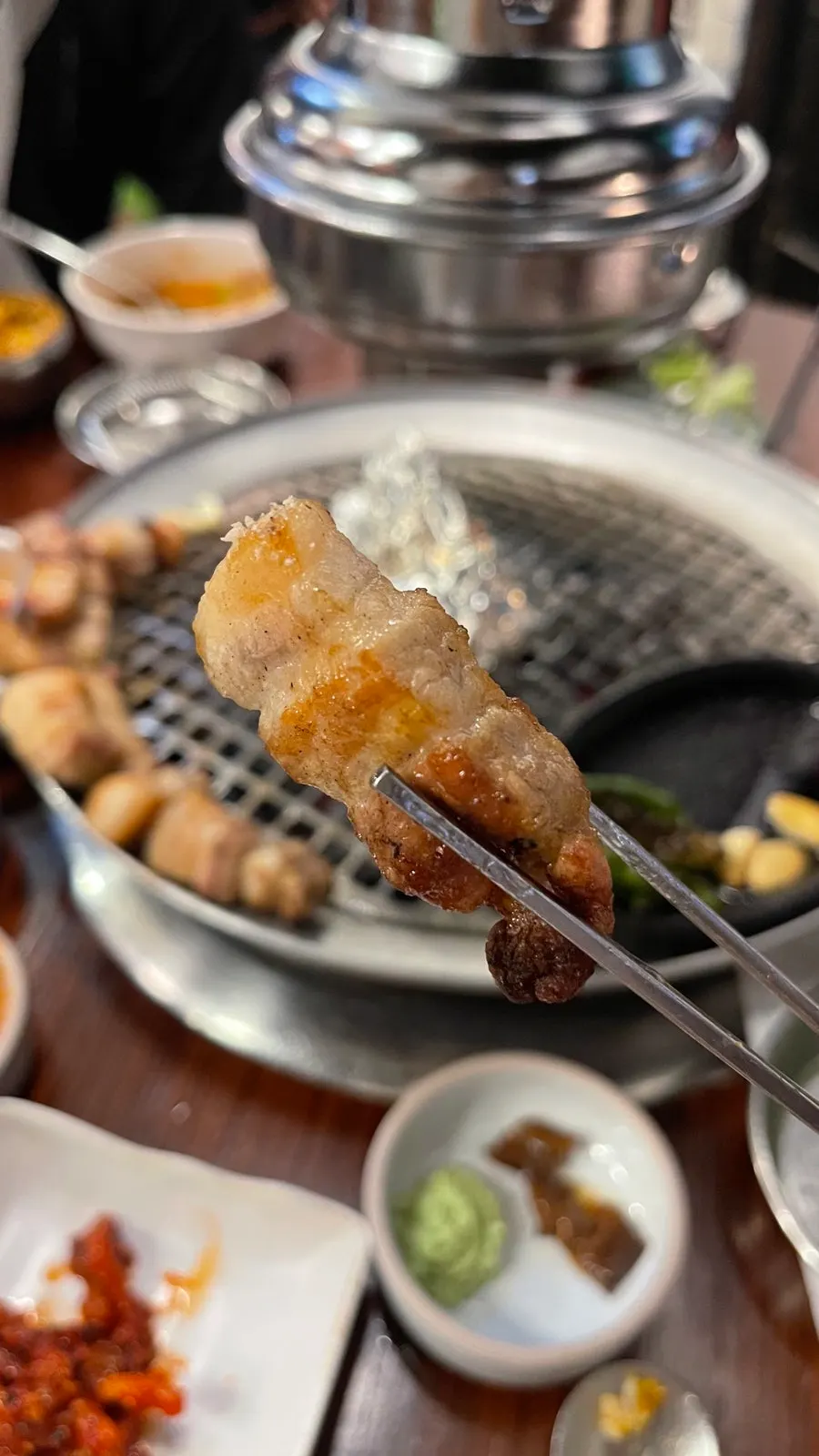 Vertical photo of whole pork belly cooking over charcoal