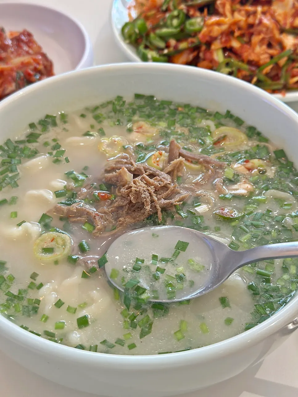 Korean beef bone kalguksu topped with green onion and beef