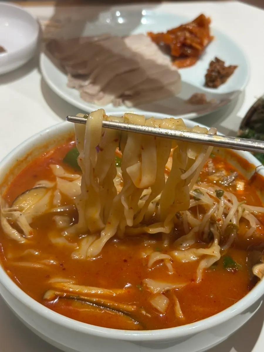Wide flat noodles soaking in yukgaejang kalguksu broth