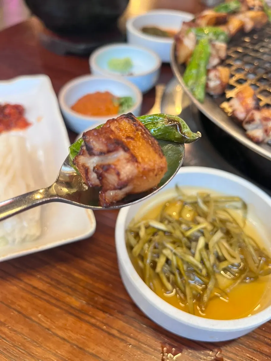 A piece of grilled pork jowl picked up with chopsticks