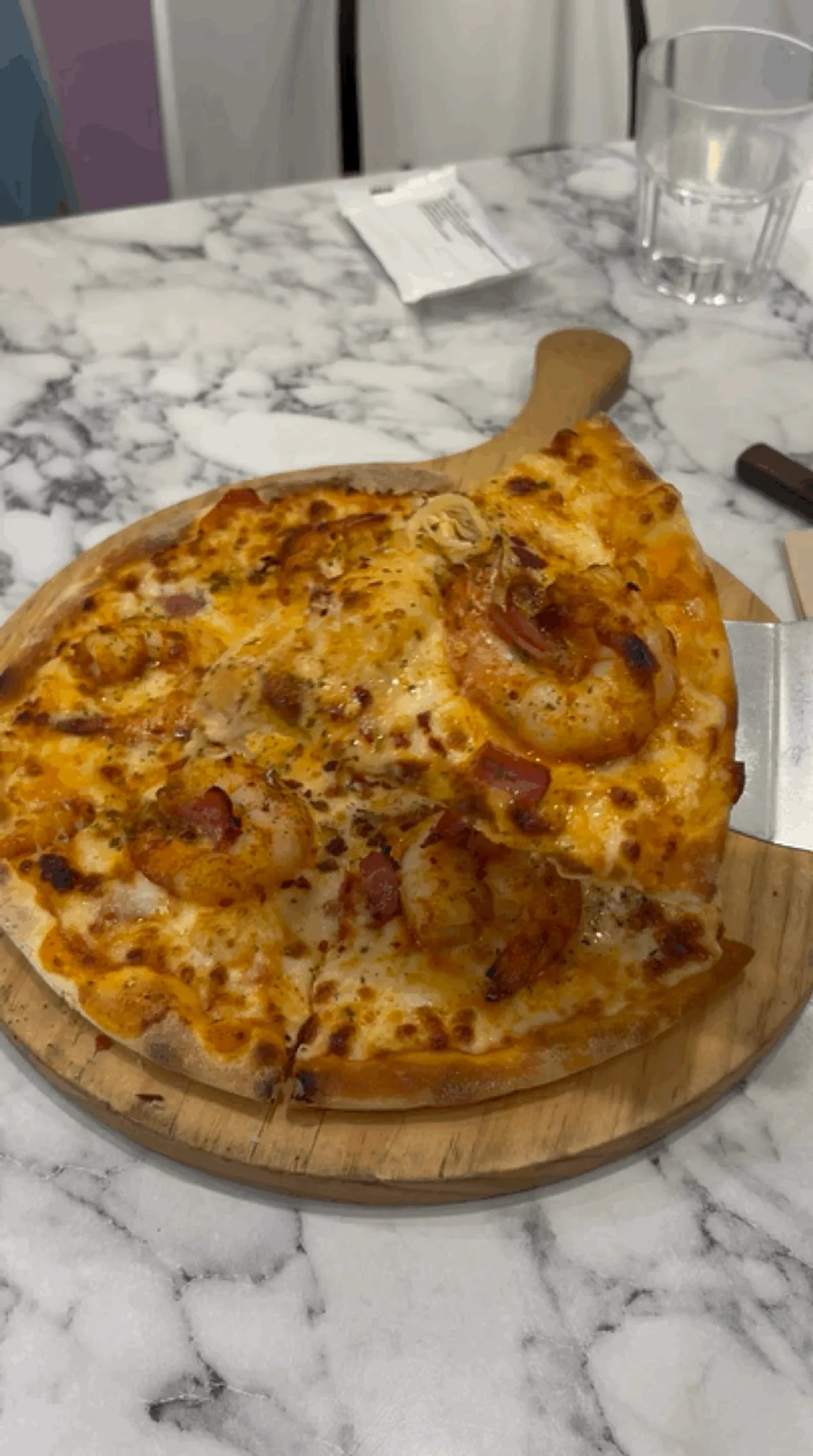 A slice of shrimp rosé pizza topped with shrimp and bacon