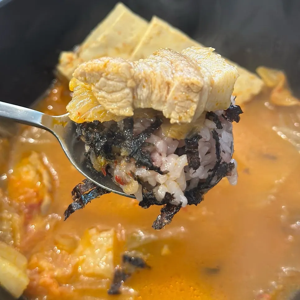 A spoonful topped with kimchi, meat, and tofu