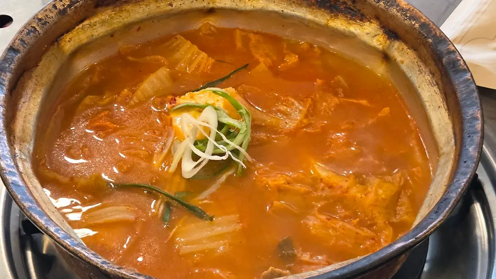 Kimchi jjigae and ramyeon sari served in a brass pot