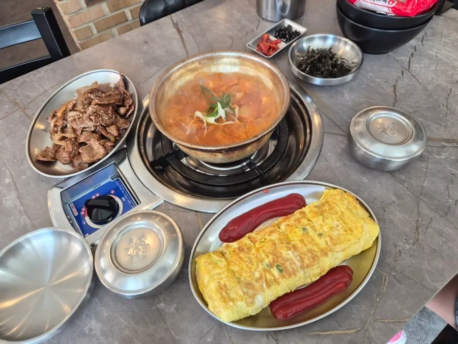 Kimchi jjigae with soy bulgogi and egg roll on the table