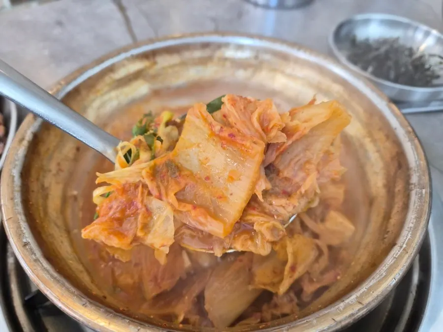 Kimchi jjigae with added ramyeon noodles in the metal bowl