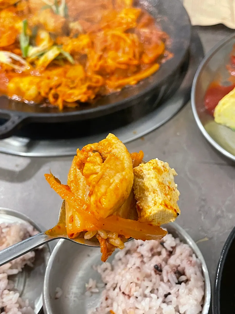 A spoon topped with a piece of kimchi jjim meat and kimchi