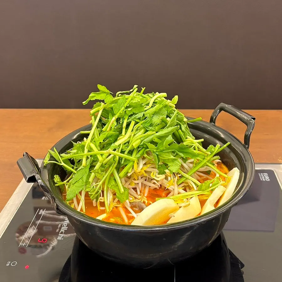 Spicy mushroom shabu hot pot topped with minari and bean sprouts