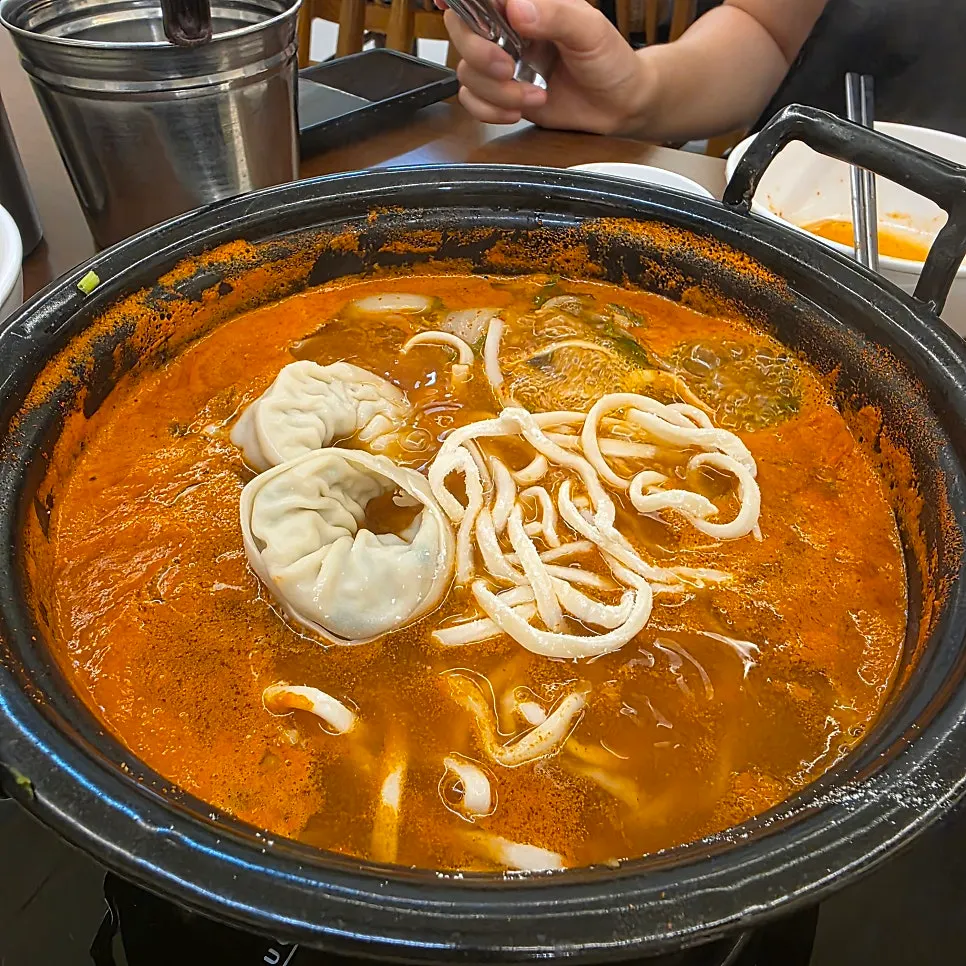 Pot of spicy mushroom kalguksu piled high with minari