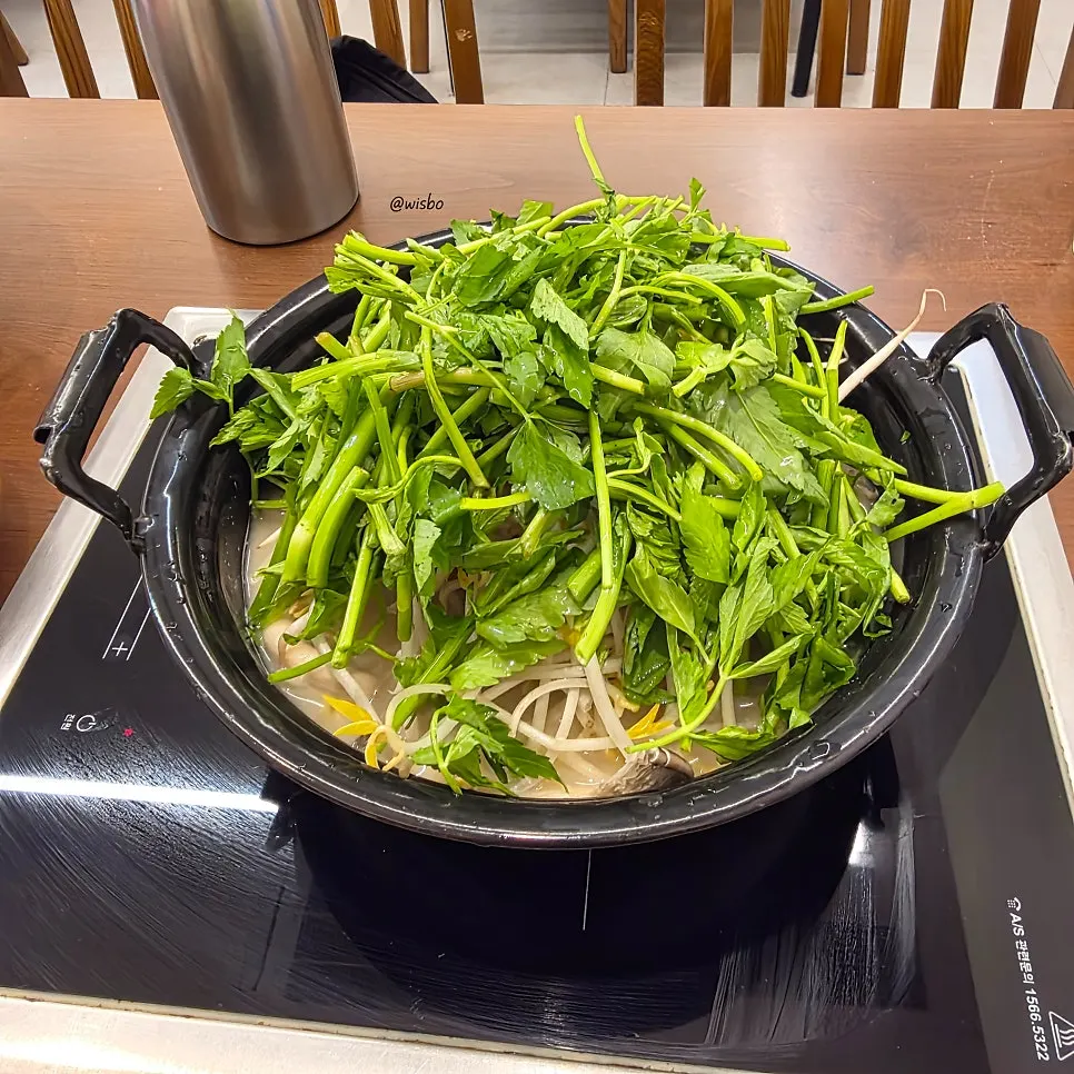 Pot of perilla broth piled high with minari and bean sprouts